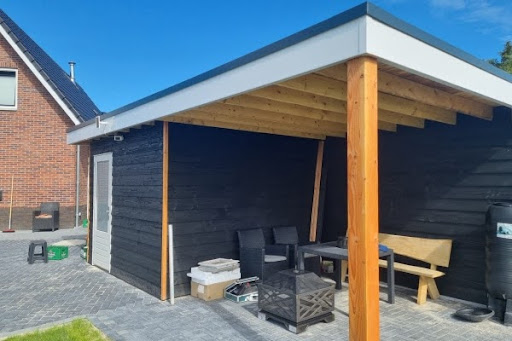 Zwarte prefab schuur met houten overkapping en zitgedeelte naast het huis