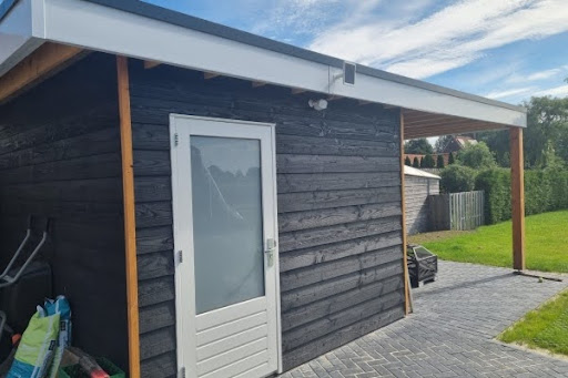 Zwarte prefab schuur met witte deur en houten accenten in een groene tuin