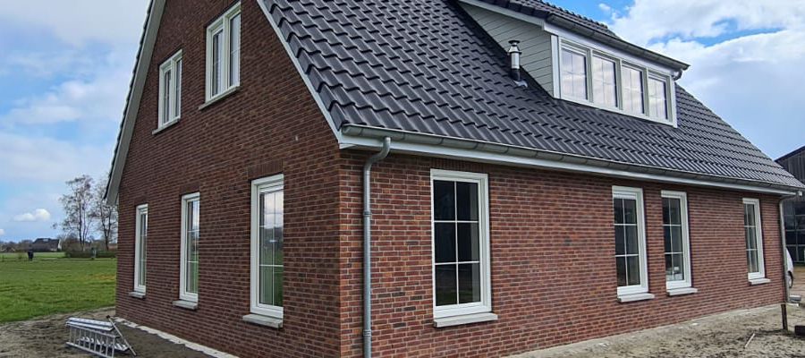 Nieuwbouwwoning met traditionele bakstenen gevel en witte kozijnen en zonnepanelen.