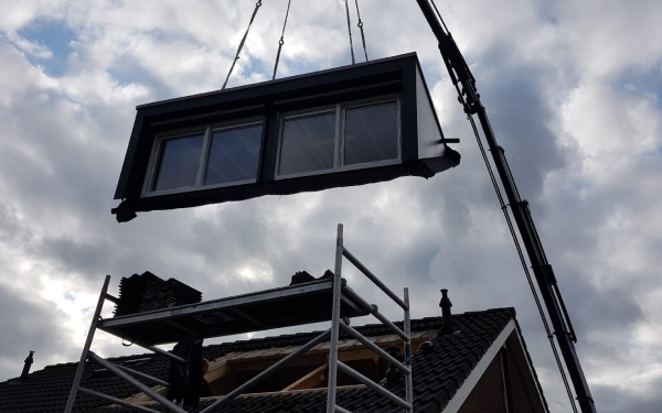 Een prefab dakkapel wordt met een kraan op een woning geplaatst